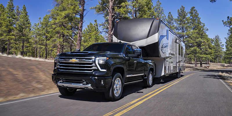 A black Chevrolet Silverado towing a large RV trailer along a scenic road through the forest.