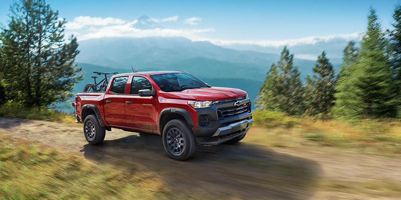 A red Chevrolet Colorado driving off-road through a scenic mountain landscape.