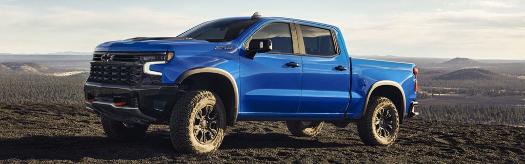 Blue Chevrolet Silverado 1500 pickup truck parked on rugged terrain with a mountainous background