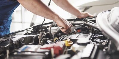 A close-up of a mechanic's hands using a tool to perform maintenance on a car engine.