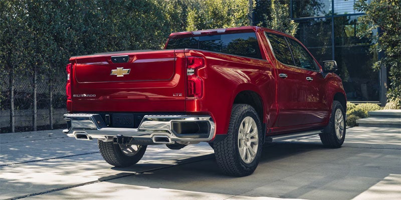 Rear view of a red Chevrolet Silverado LTZ pickup truck parked in a paved driveway outside a modern building.
