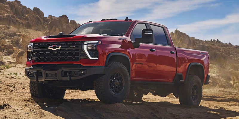 A red Chevrolet Silverado HD ZR2 pickup truck parked on a desert trail surrounded by rocky hills.